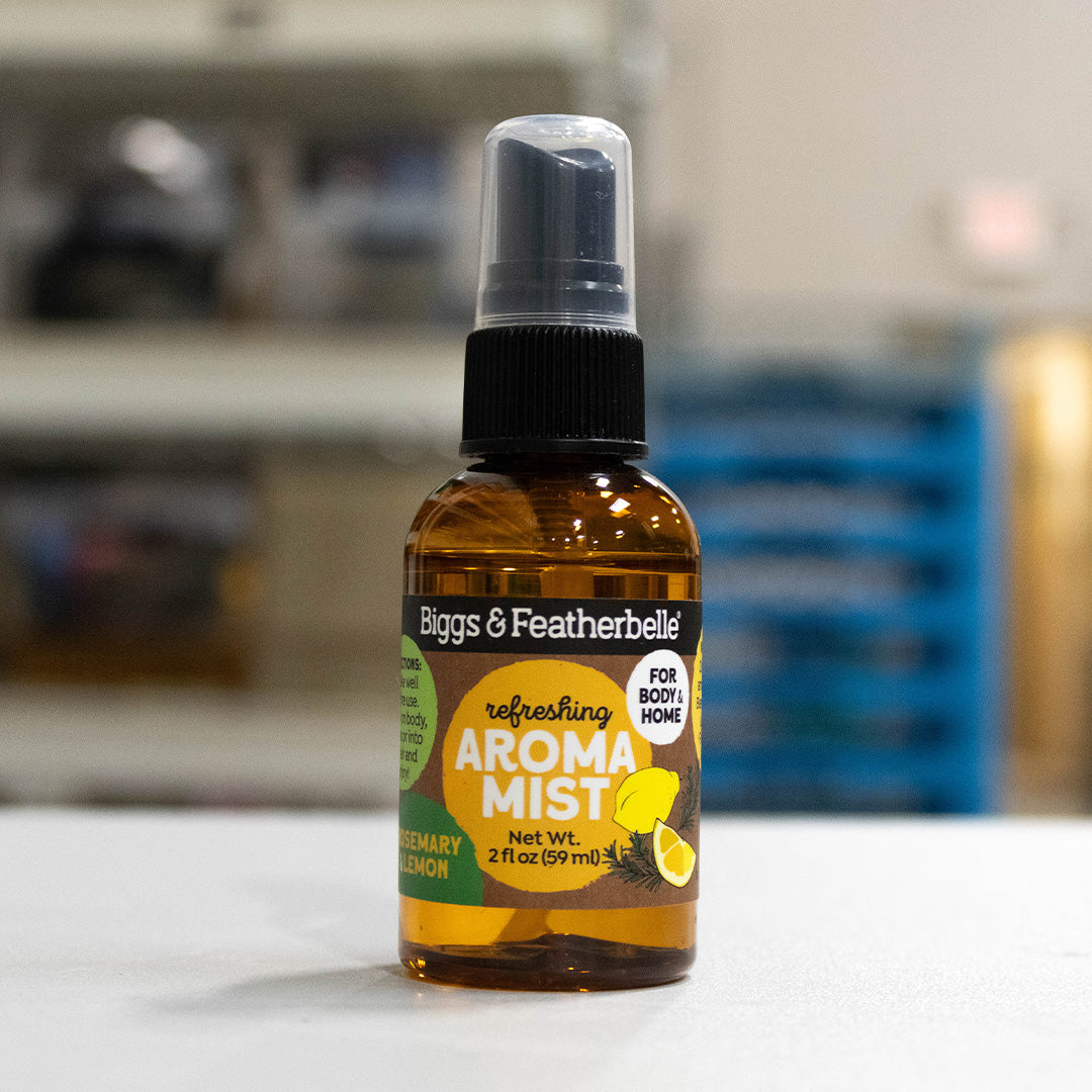 A bottle of Biggs & Featherbelle Freshing Aroma Mist in German Lemon scent, featuring an amber glass bottle with a black spray cap and a green and yellow label, set against a blurred background.