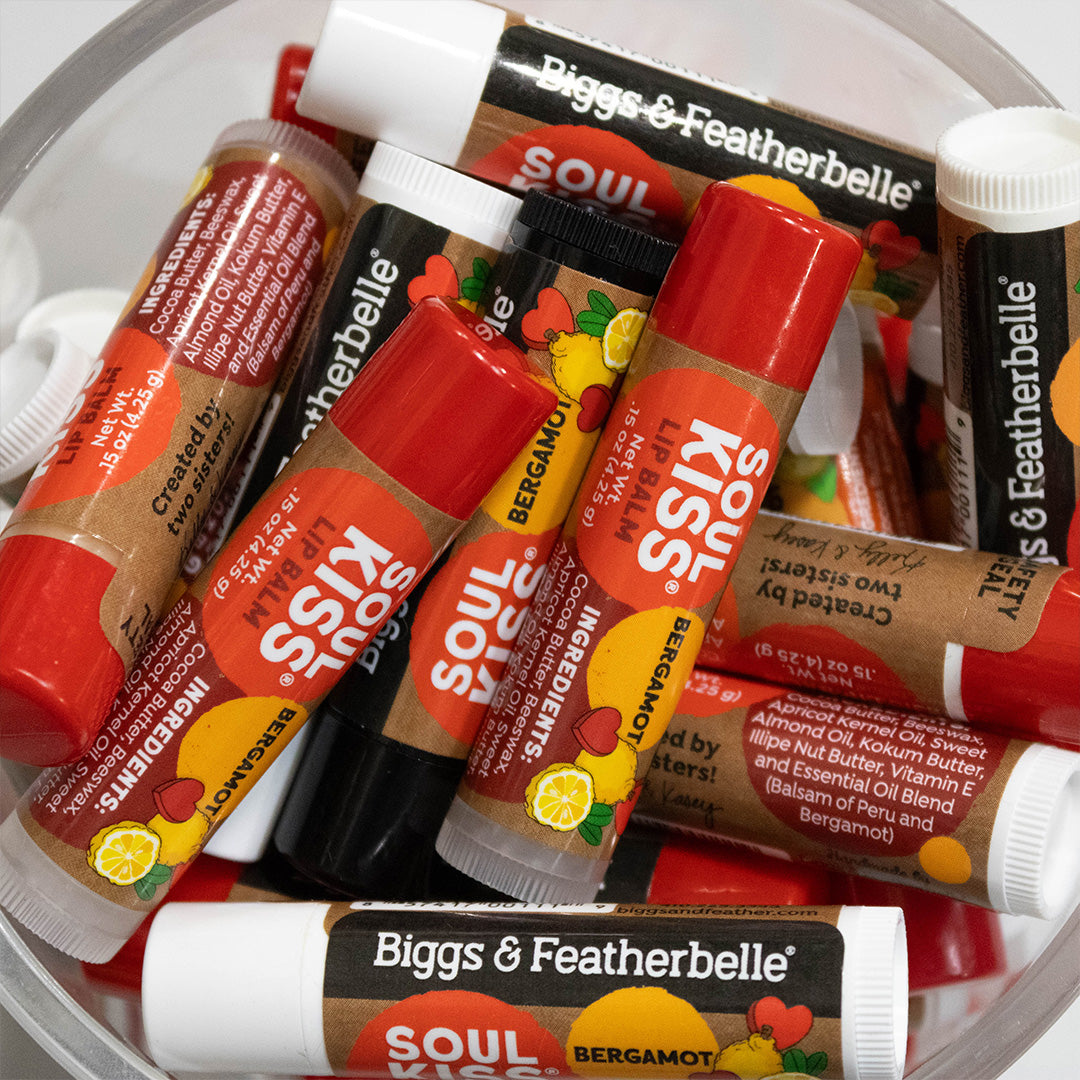 A close-up of multiple Biggs &amp; Featherbelle Soul Kiss lip balm tubes in different flavors, including Bergamot, Lemon, and Sesame, arranged inside a clear plastic tub.