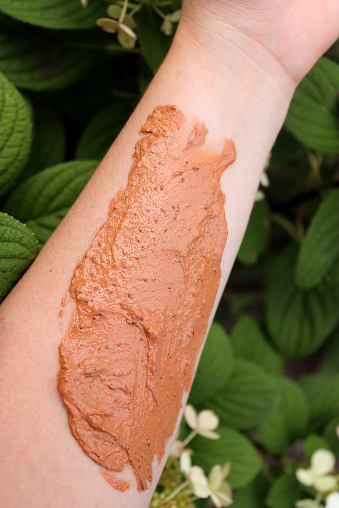 Cedar Soap Scrub applied to a person's arm with green leaves in the background