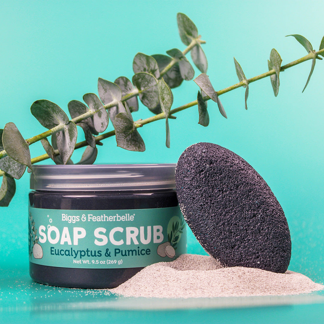 Jar of soap scrub with a pumice stone and eucalyptus leaves on a teal background